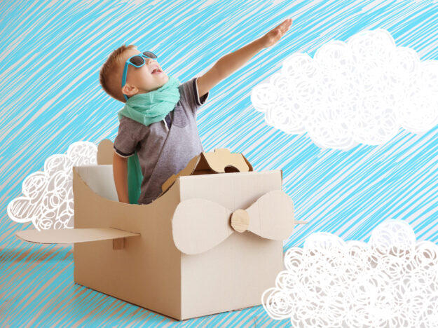 Little boy playing with cardboard airplane on white wall backgro